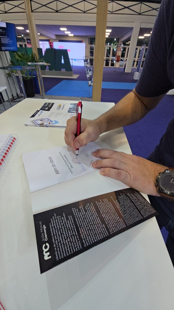 Mão de João Marcel Camargo autografando o livro Além do Óbvio