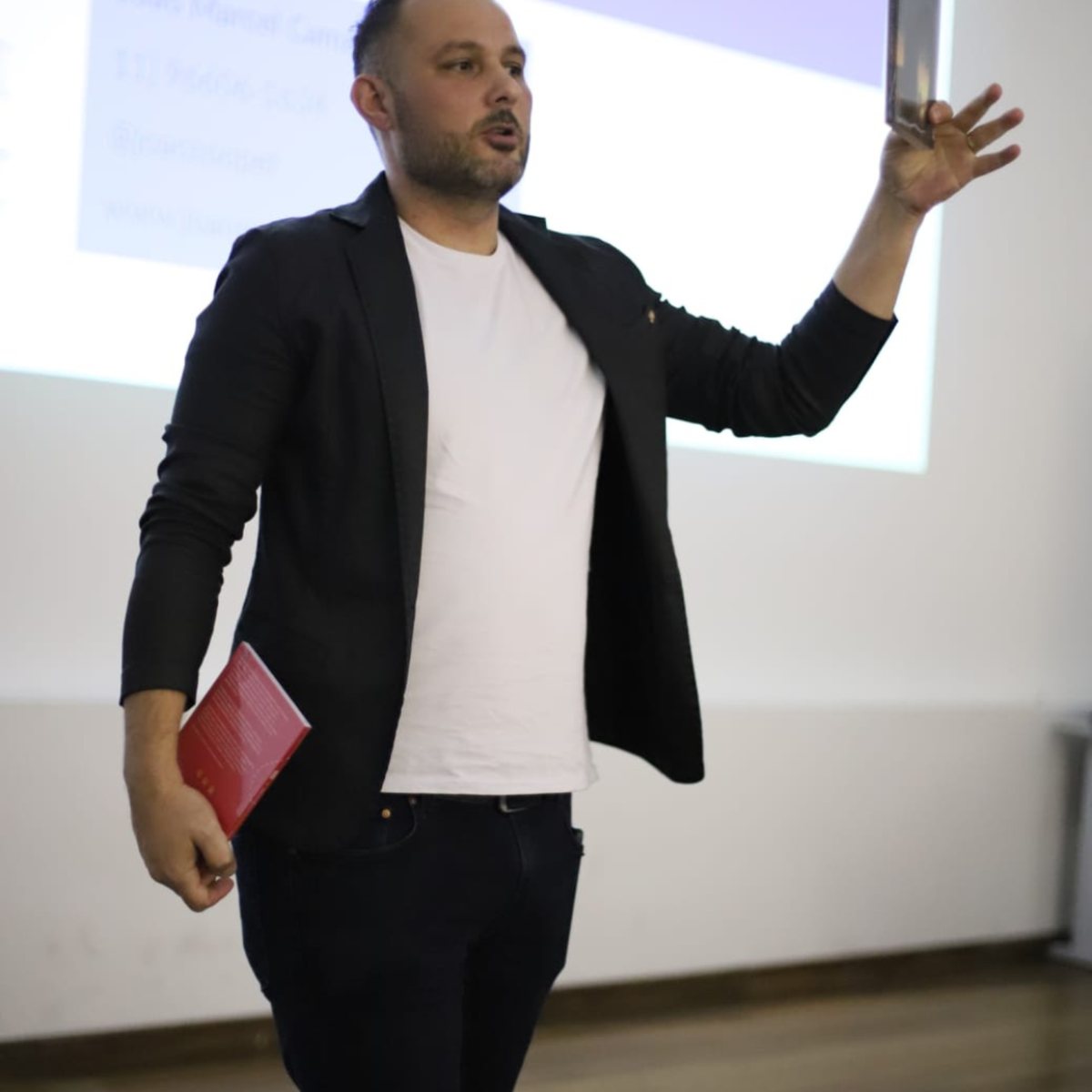 João Marcel Camargo dando uma palestra, com um livro na mão